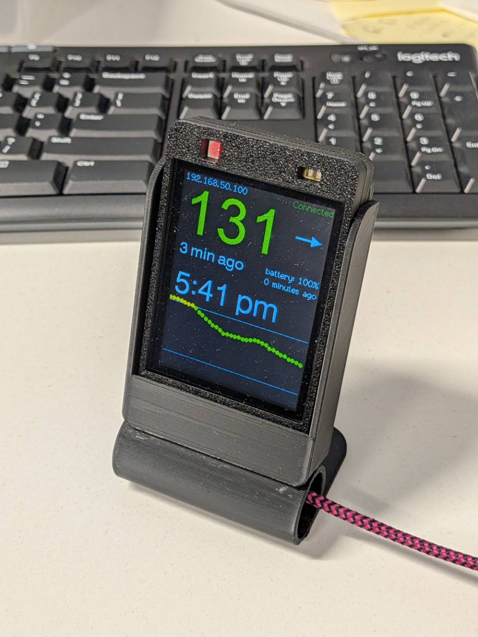 A compact glucose display in a dark printed enclosure on a desk